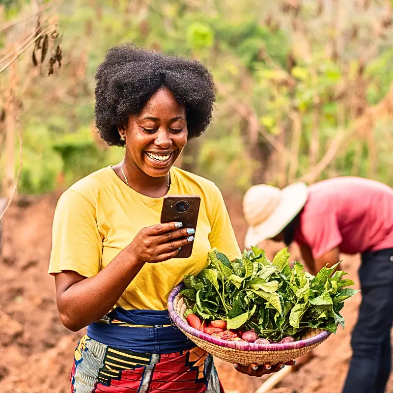 monetize-farm-data-with-blockchain-farmer-mobile-tech A farmer in the field holding fresh produce and using a smartphone to manage farm data, illustrating blockchain-powered agricultural workflows.