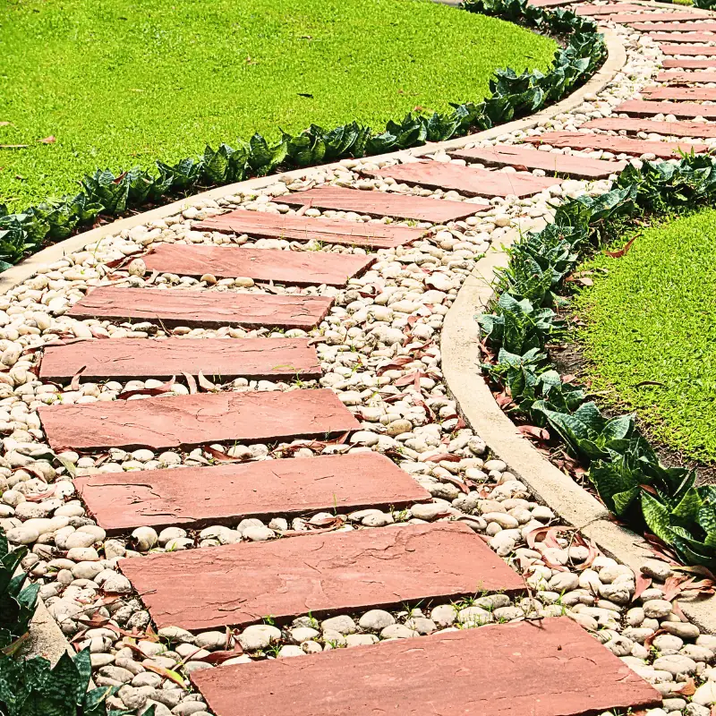 Curved garden path made of rectangular brick tiles set in white pebbles, bordered with green edging plants—ideal for space-saving garden layouts.